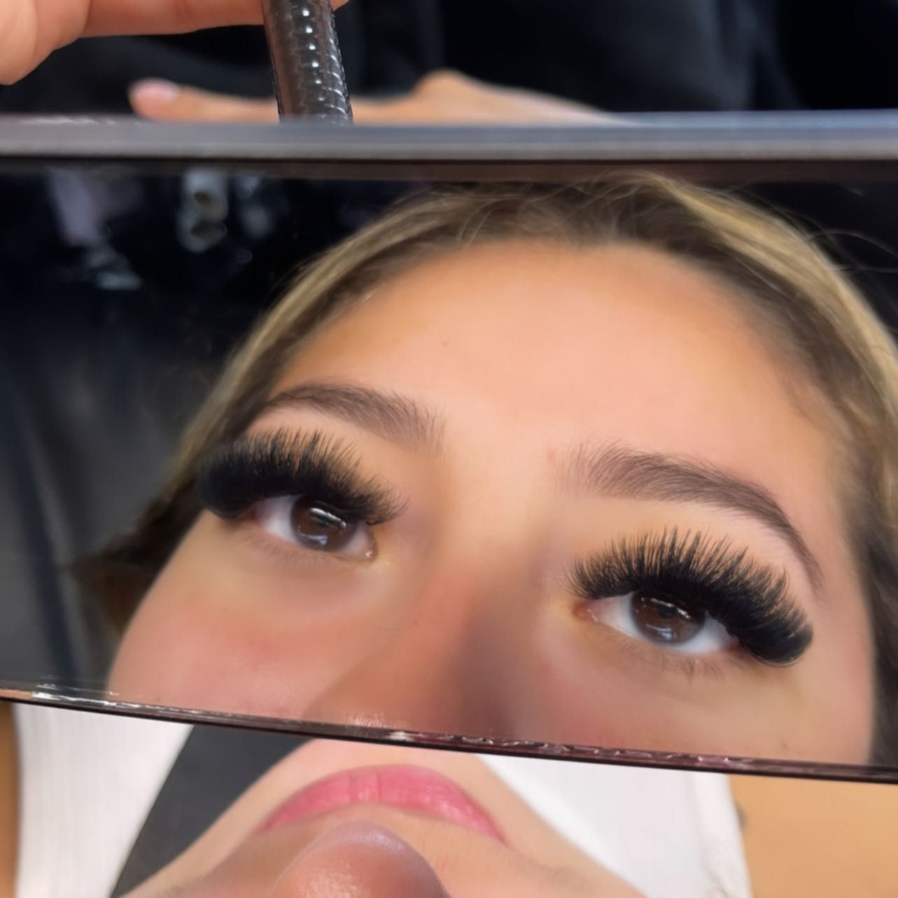 Client seeing her new lashes in a hand mirror